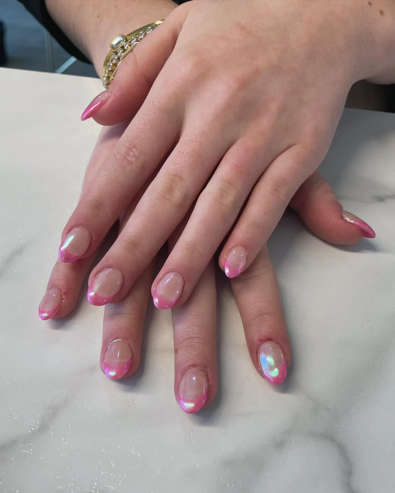Deux mains posées sur un comptoir de marbre, ongles amande avec une french rosée nacrée.