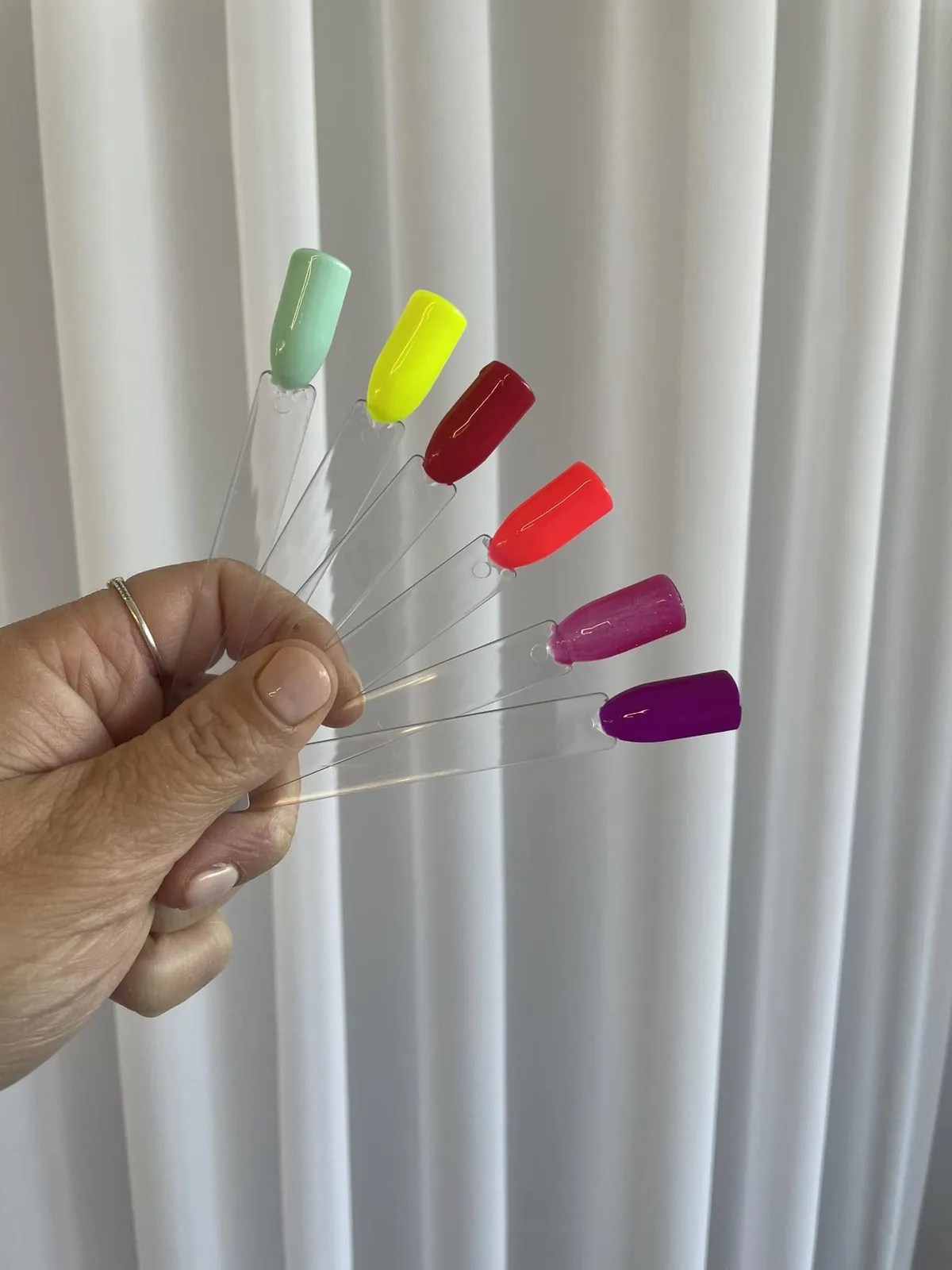 Une main tient en éventail six bâtonnets d’essai de vernis, chacun d’une teinte différente.